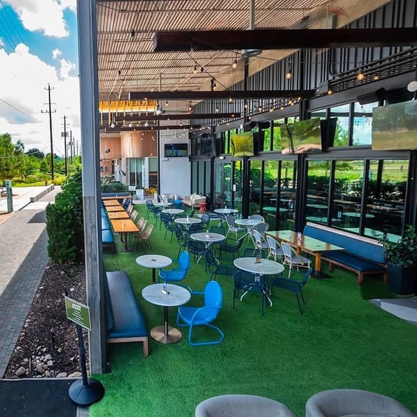 Highline Park's outdoor patio with artificial turf, various tables, blue chairs, and large windows.