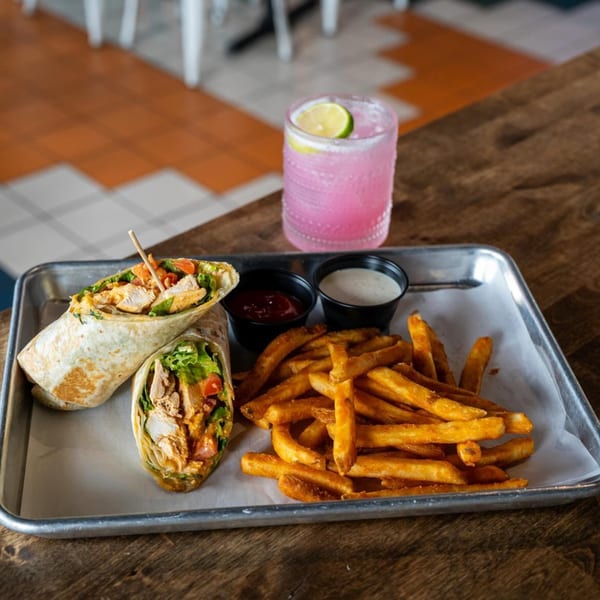 Highline Park's chicken wrap with fries, dipping sauces, and a pink cocktail with a lime.