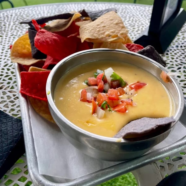 Highline Park's queso dip with pico de gallo, served with colorful tortilla chips on a metal tray.