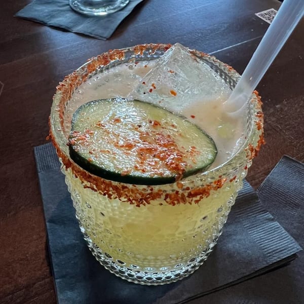 A Highline Park margarita with a chili-lime rim, ice, a straw, and a cucumber slice.