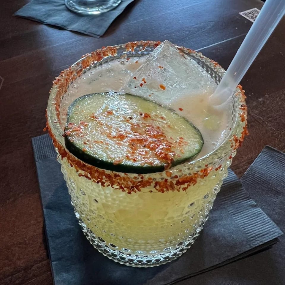 A Highline Park margarita with a chili-lime rim, ice, a straw, and a cucumber slice.