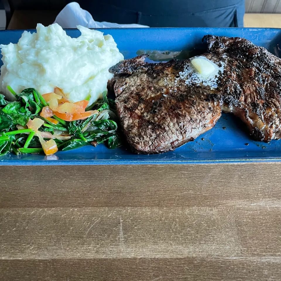 Grilled steak with a pat of butter, mashed potatoes, and sautéed spinach on a blue plate.