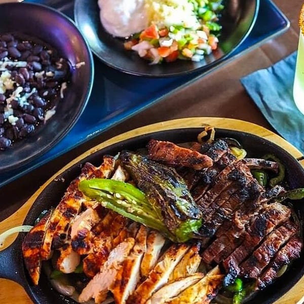 Sizzling fajitas with chicken, steak, peppers, and onions, served with black beans and salsa.