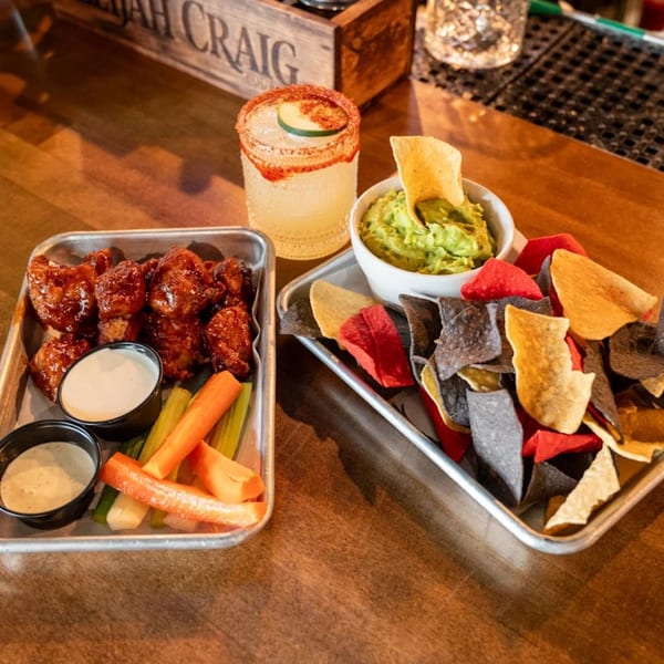 Highline Park's chicken wings, guacamole with colorful chips, and a cocktail on a wooden bar.