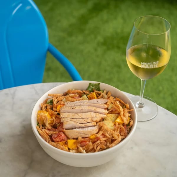 Highline Park's chicken salad with crispy toppings and a glass of white wine on a marble table.