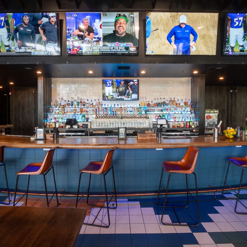 A bar at Highline Park with multiple TVs showing sports, a full liquor display, and bar stools.