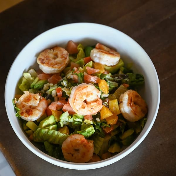 Highline Park's shrimp salad with lettuce, avocado, tomatoes, and oranges in a white bowl.