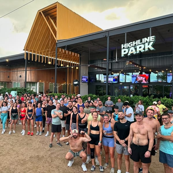 A large group of people gathered in front of Highline Park bar-&-grill, with a modern building and outdoor screens.