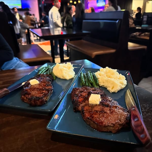 Two plates of steak, mashed potatoes, and green beans on a table at Highline Park.