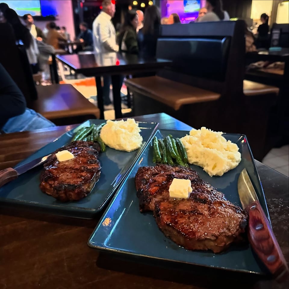 Two plates of steak, mashed potatoes, and green beans on a table at Highline Park.