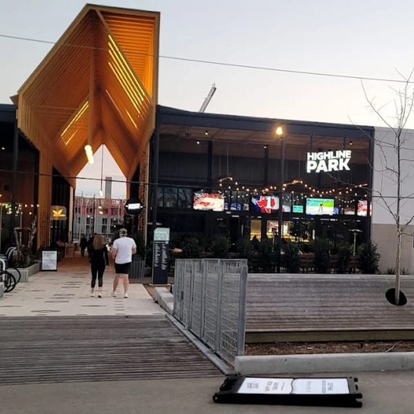 Exterior of Highline Park bar-&-grill with a modern wooden entrance, outdoor seating, and people walking by.