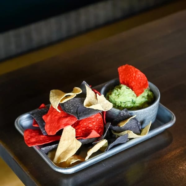 Colorful tortilla chips in red, black, and yellow with a side of guacamole on a metal tray.