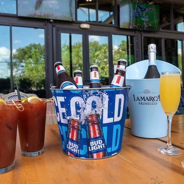 A bucket of Bud Light beers, Bloody Marys, and a mimosa on an outdoor bar table.