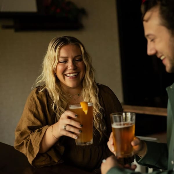 Two people smiling and clinking glasses of beer at Highline Park bar-&-grill.