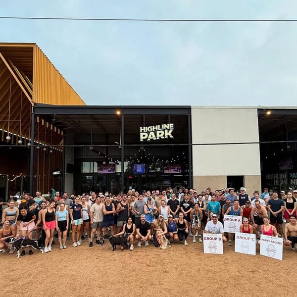 A large group of people and dogs stand in front of Highline Park bar-&-grill, holding signs.