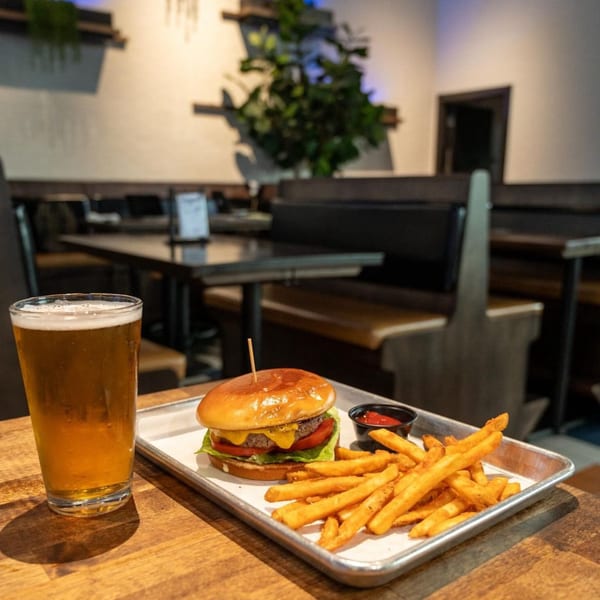 Highline Park's cheeseburger and fries with a beer on a wooden table in a restaurant setting.