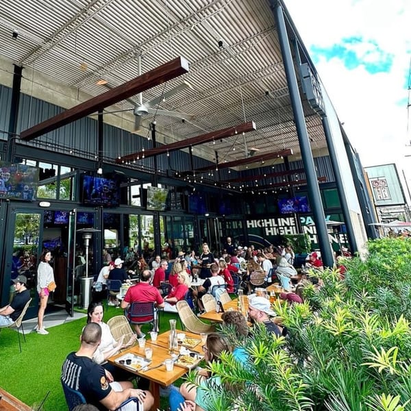 Highline Park's outdoor patio is bustling with patrons enjoying food and drinks under a large awning.